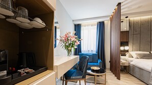 A modern hotel room with a dining area, a sofa, a bed, and a vase of flowers. - Caldo Luxury Rooms (Split)