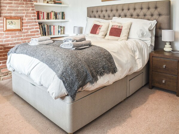 A bedroom with a bed, bedside tables, a lamp, a bookshelf, and a brick wall.