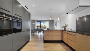 Eine moderne Küche mit grauen Schränken, Holz Arbeitsplatten und einer zentralen Kochinsel. Über der Insel hängen Pendelleuchten und ein großes Fenster sorgt für natürliches Licht.