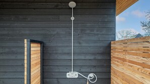 Eine moderne Außendusche mit Holzumrandung, einem Metallschlauch und einer Bedienkonsole.