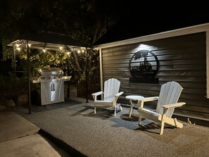 Un patio al aire libre con una parrilla, dos sillas Adirondack y una mesa.