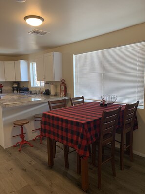 Un comedor con mantel a cuadros rojo y negro, sillas de madera y una ventana con persianas.