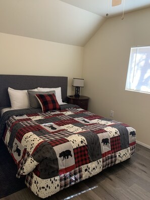 Un dormitorio con una cama grande, una mesita de noche, una lámpara y una ventana.