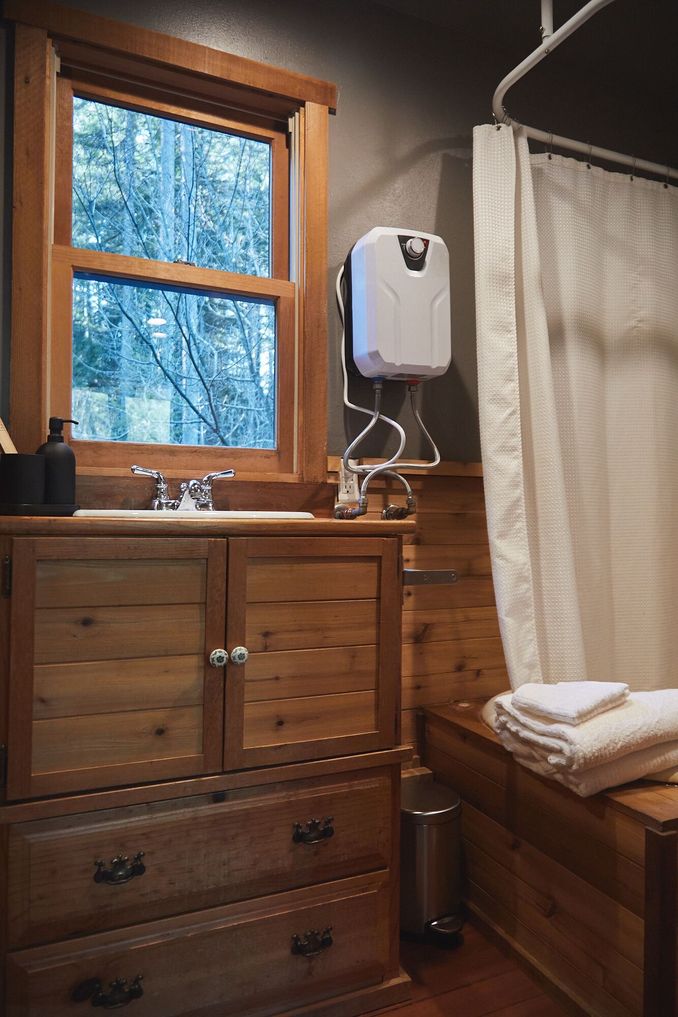 A wooden bathroom with a window, a sink, a towel rack, and a shower curtain.