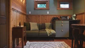 Een gezellige kamer met een houten wand, een groene bank, een kleine tafel en een kast met een magnetron.