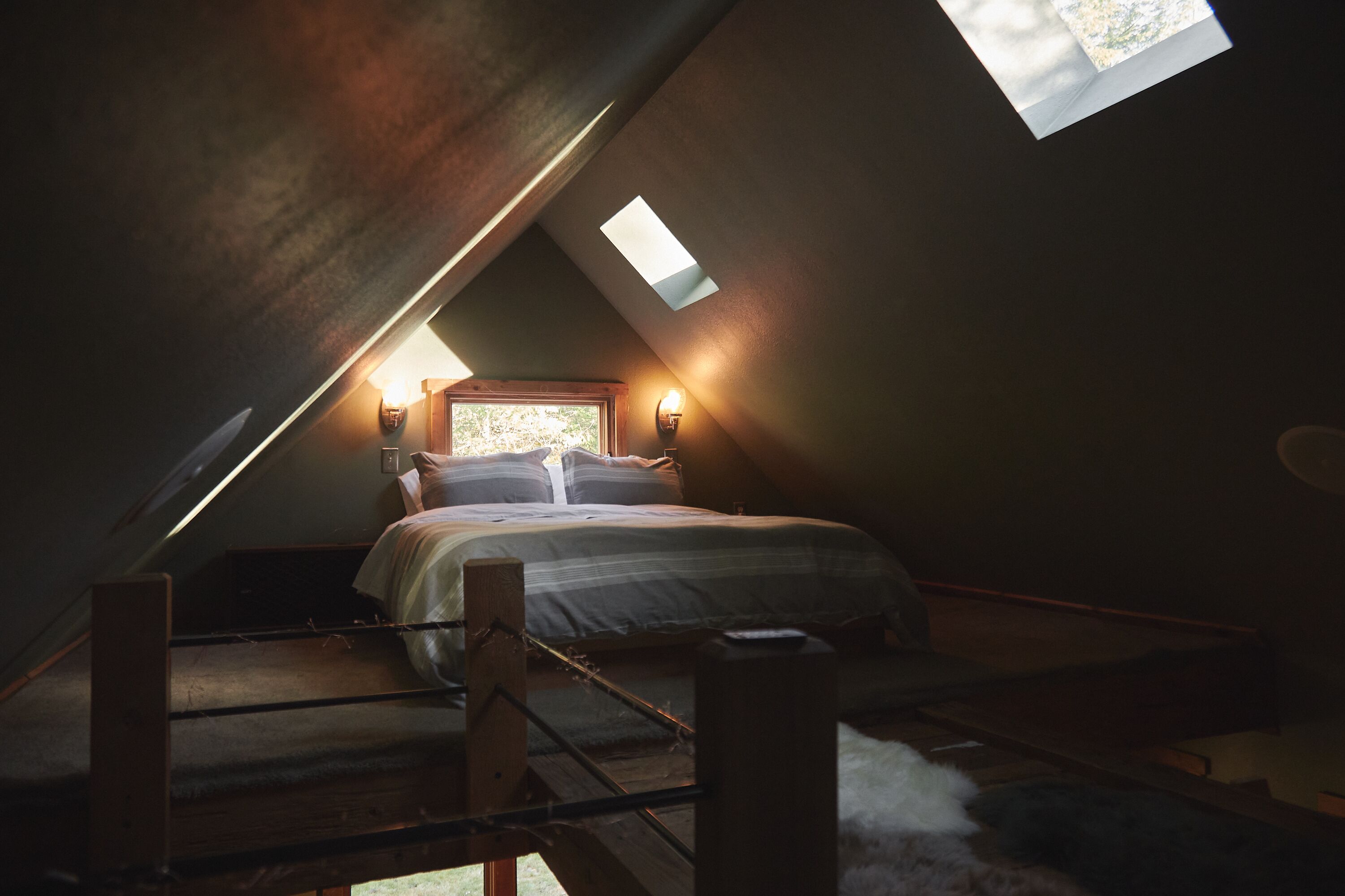 Une chambre confortable située sous les toits, avec un plafond en pente, un lit avec des oreillers, une table de chevet et une lampe fixée au mur.