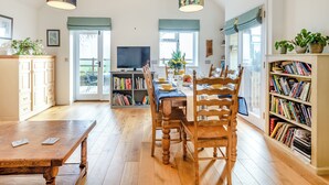A dining area with a wooden table, chairs, a bookshelf, and a television. - 1 bedroom accommodation in Diss (Diss)