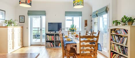 A dining area with a wooden table, chairs, a bookshelf, and a television.
