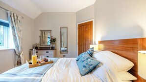 Ein Schlafzimmer mit Bett, Nachttisch, Kommode, Spiegel und einem Fenster mit Vorhängen.