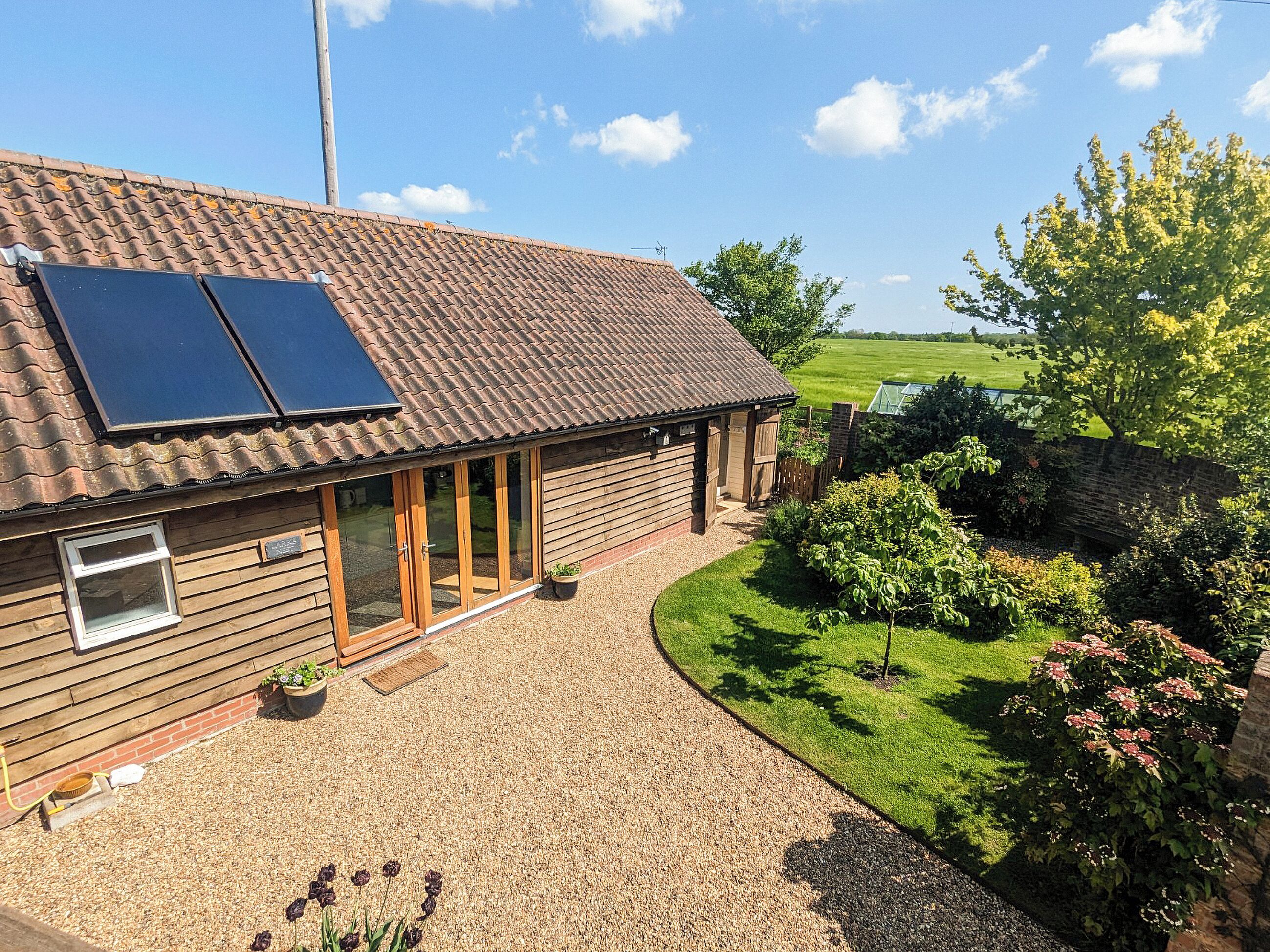A wooden house with solar panels, a gravel driveway, and a garden.