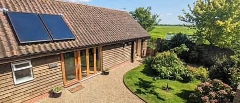 A wooden house with solar panels, a gravel driveway, and a garden.