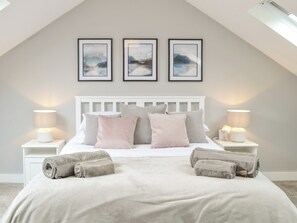 A bedroom with a white headboard, three framed artworks on the wall, two bedside lamps, and a neatly made bed with rolled towels. - 1 bedroom accommodation in Brampton (Brampton)