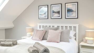A bedroom with a sloped ceiling, a white bed with multiple pillows, two bedside tables with lamps, and three framed pictures on the wall.