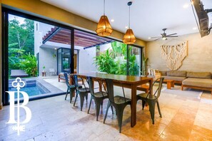 A modern dining area with a glass wall, a pool, and outdoor plants.
