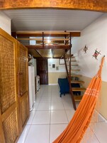 Quarto com teto de madeira, rede, escada e área de cozinha.