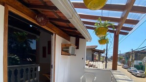 A covered patio with a white chair, a glass door leading inside, and hanging planters. - Casas Vasconcelos (Itacaré)