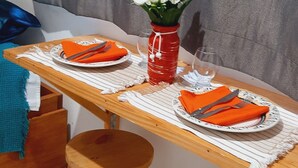 A dining table with two stools, a red vase with white flowers, and orange napkins. - Casas Vasconcelos (Itacaré)