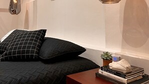 A bedroom with a bed, two hanging pendant lights, a framed picture on the wall, and a nightstand with books and a small plant. - Hotel Atia (Guadalajara)