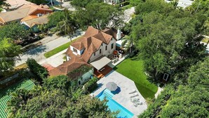 Et luftfoto af et hus med swimmingpool, omgivet af frodigt grønt og en velplejet græsplæne.