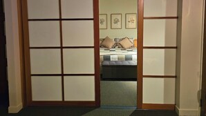 Een traditionele Japanse kamer met tatami vloeren, een bed met een geborduurde spreideken en drie ingelijste bloemwerk afbeeldingen aan de muur.