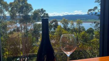 A bottle of Tasmanian Pinot Noir 2023 and a wine glass on a wooden table with a scenic view of trees and water.
