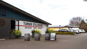 Een Turner Stillhouse gebouw met een bord waarop rondleidingen en proeverijen worden aangekondigd. Er staan potplanten en vaten buiten.