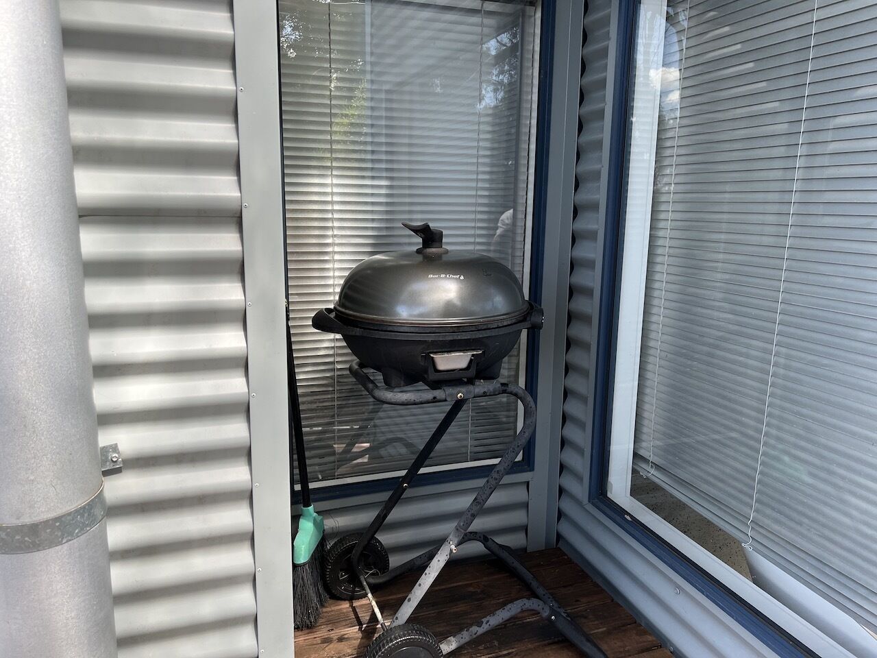 Un conjunt de barbacoa portàtil col·locat en una cantonada, amb finestra i persianes.
