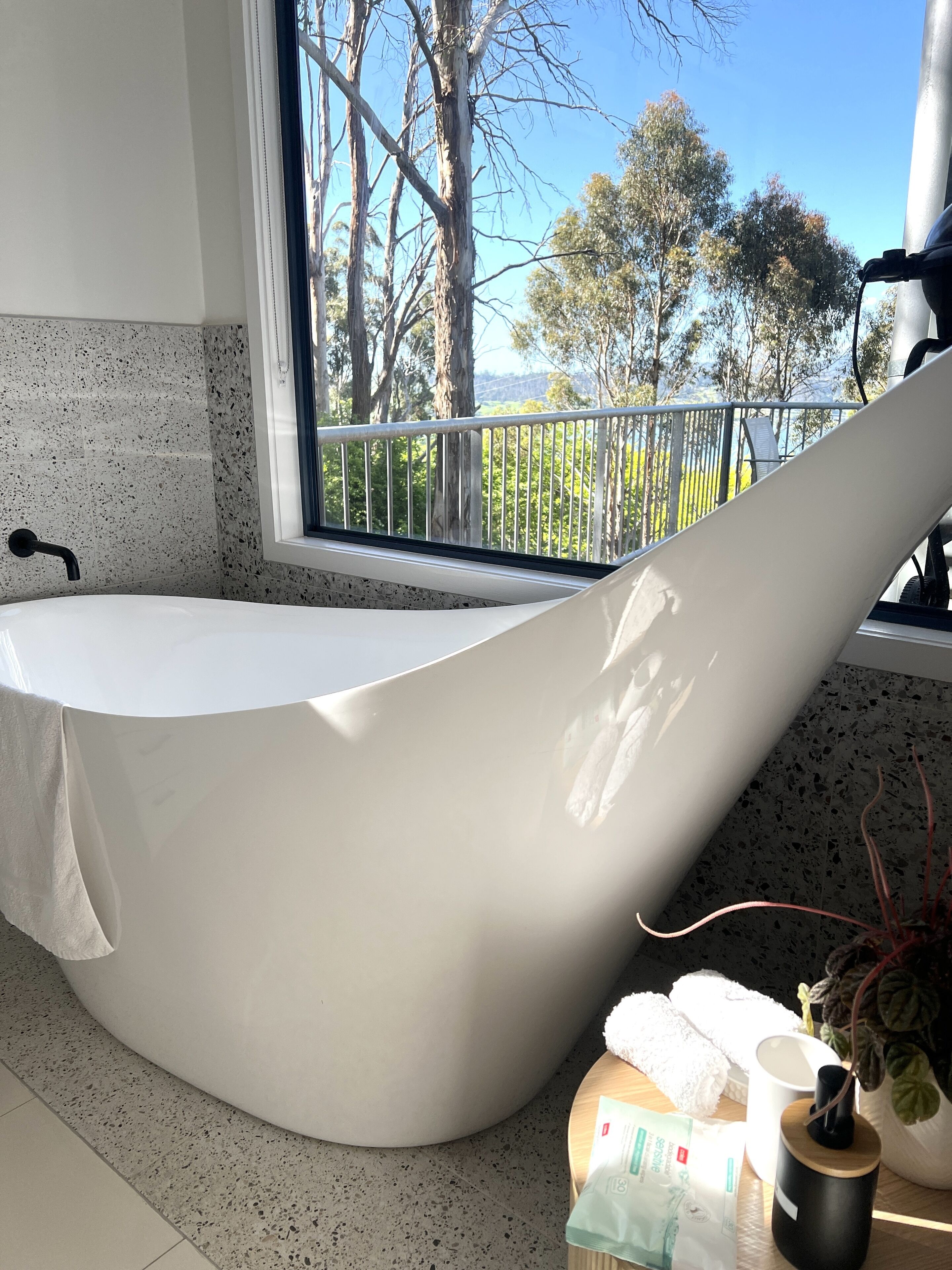 A modern bathroom with a freestanding bathtub, a window with a view of trees and a distant landscape, and a countertop with toiletries.
