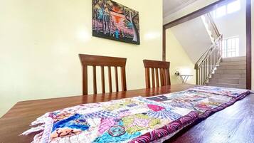 Una mesa de comedor con un colcha colorida, dos sillas de madera y un cuadro en la pared.