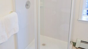 A glass-enclosed shower with a white frame, a white towel hanging on the wall, and a window to the right. - Historic Apartment in Downtown Seward (Seward)