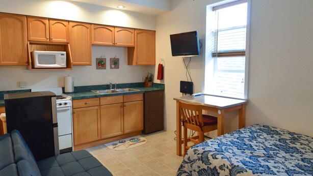A compact room with a kitchenette, a bed, a television, and a window. - Historic Apartment in Downtown Seward (Seward)