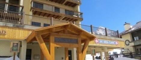 A multi-story building with a ski area sign, wooden balconies, and a covered entrance.