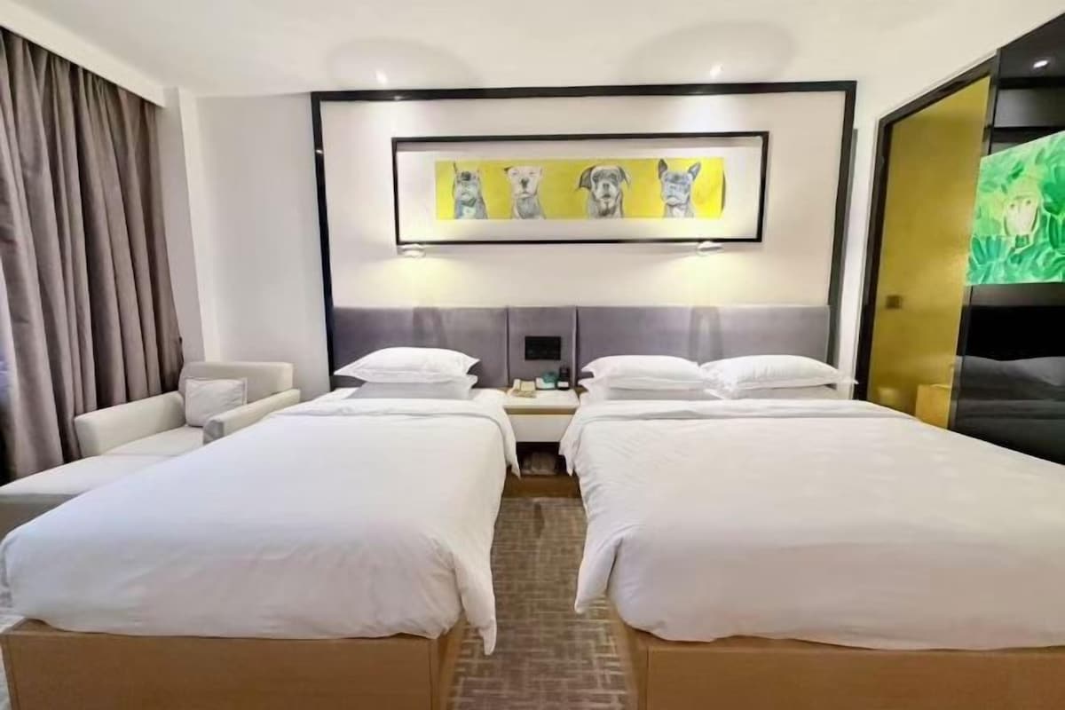 A hotel room with two beds, a desk, a chair, and a large painting on the wall.