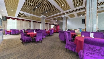 A banquet hall with purple upholstered chairs and tables, a patterned carpet, and a high ceiling with wooden beams.