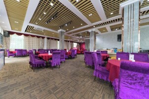 Un salón de banquetes con sillas tapizadas de color púrpura y mesas, una alfombra estampada y un techo alto con vigas de madera.