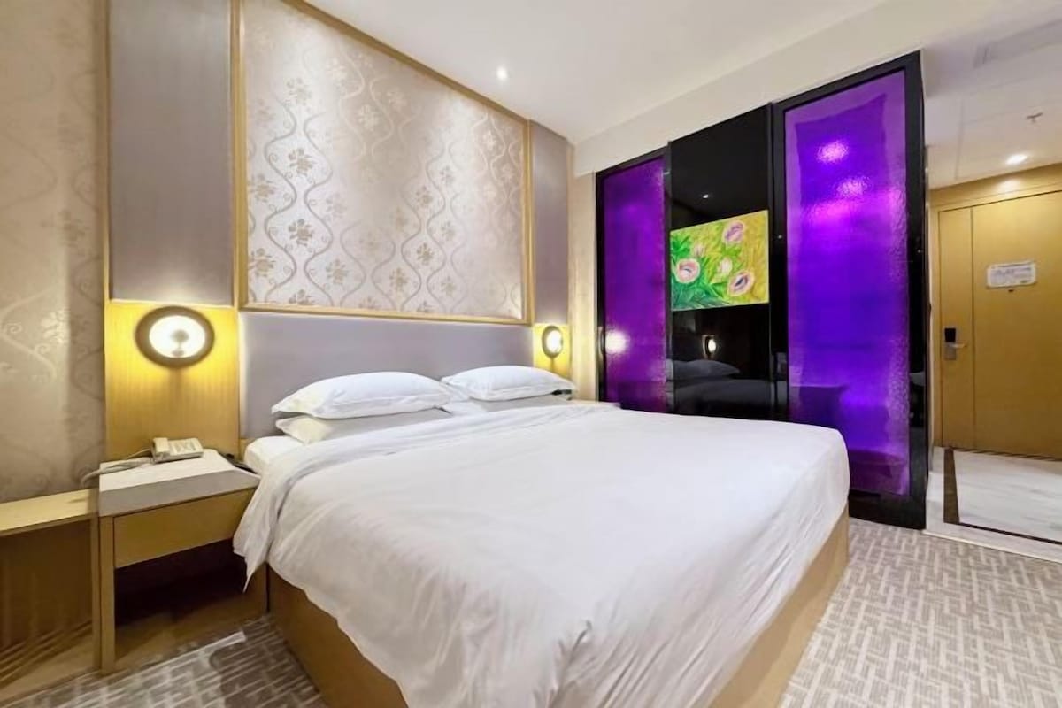 A hotel room with a bed, bedside tables, a nightstand, and a wall-mounted light fixture.