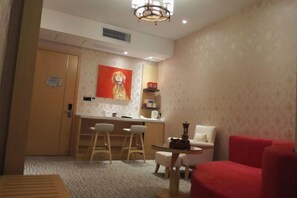 A hotel room with a dining area, a red armchair, a small table, and a painting on the wall. - Weiyina Hotel (Renhua)