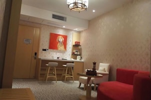 Habitación de hotel con zona de comedor, un sillón rojo, una mesita y un cuadro en la pared.