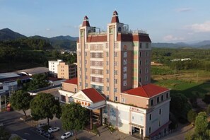 A multi-story hotel with a central tower, surrounded by greenery and mountains.