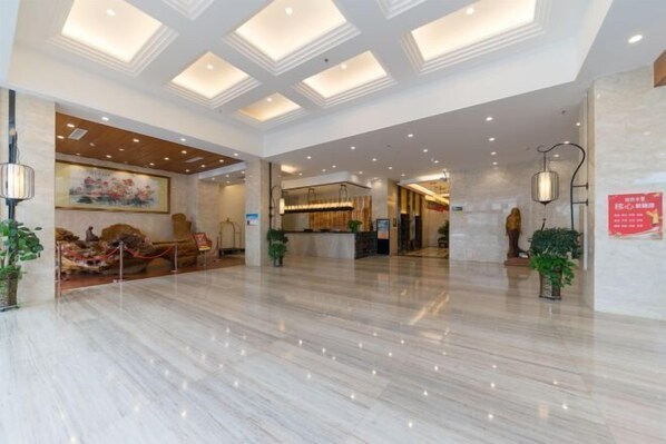 A spacious lobby with a marble floor, recessed lighting, and a reception area with a counter and chairs.