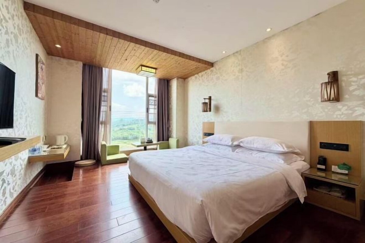 A hotel room with a large bed, a desk with a chair, a TV, and a window with curtains.