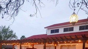 Um alpendre coberto com luzes de fada, uma pérgola e um candeeiro suspenso.