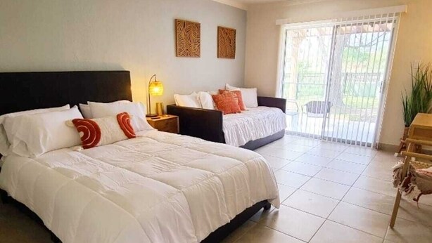 Quarto de hotel com duas camas, uma mesa de cabeceira com abajur e vista para o exterior através de uma porta de correr de vidro.