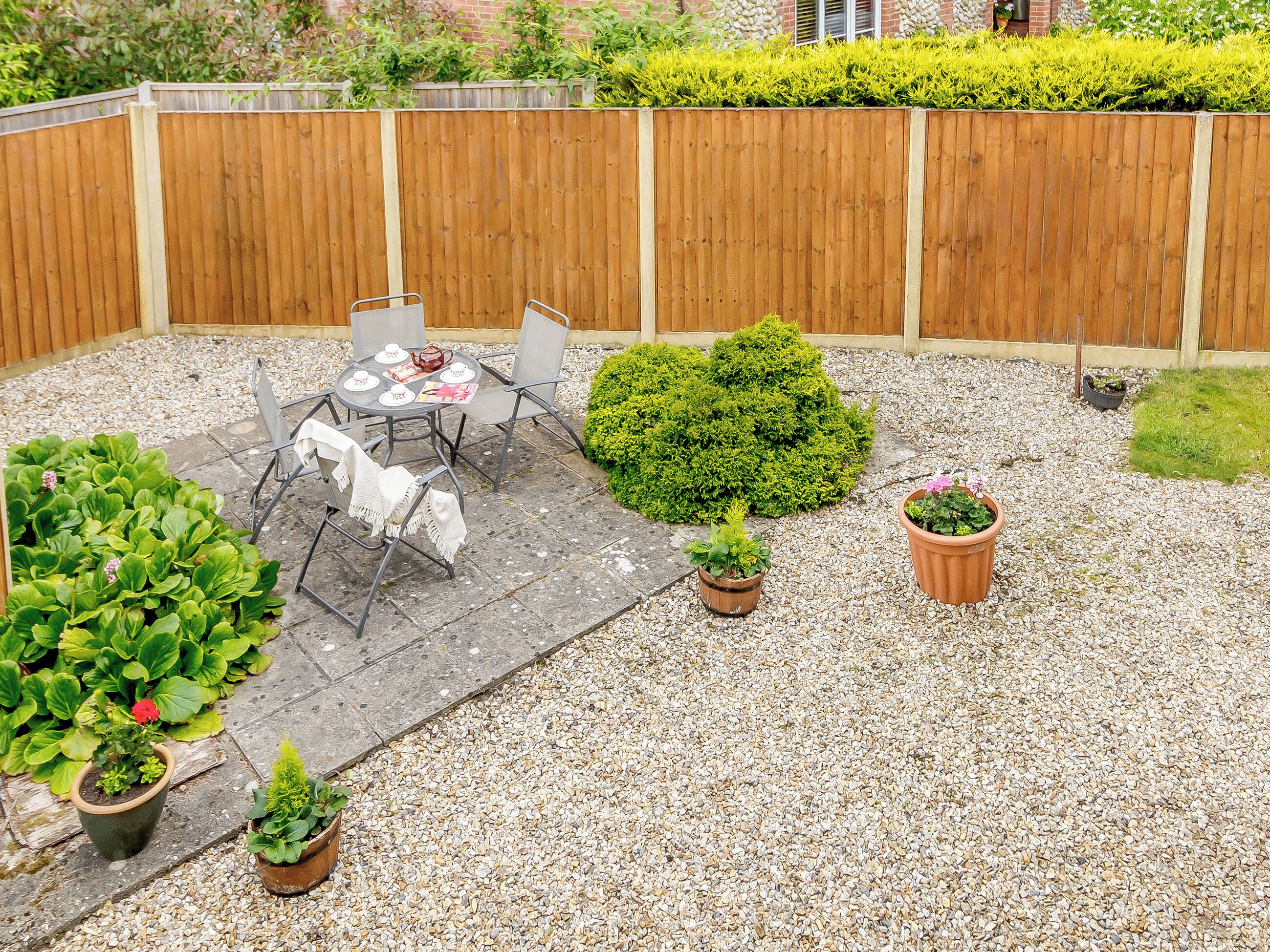 En terrasse med bord og stole, omgivet af krukker med planter og et træhegn.