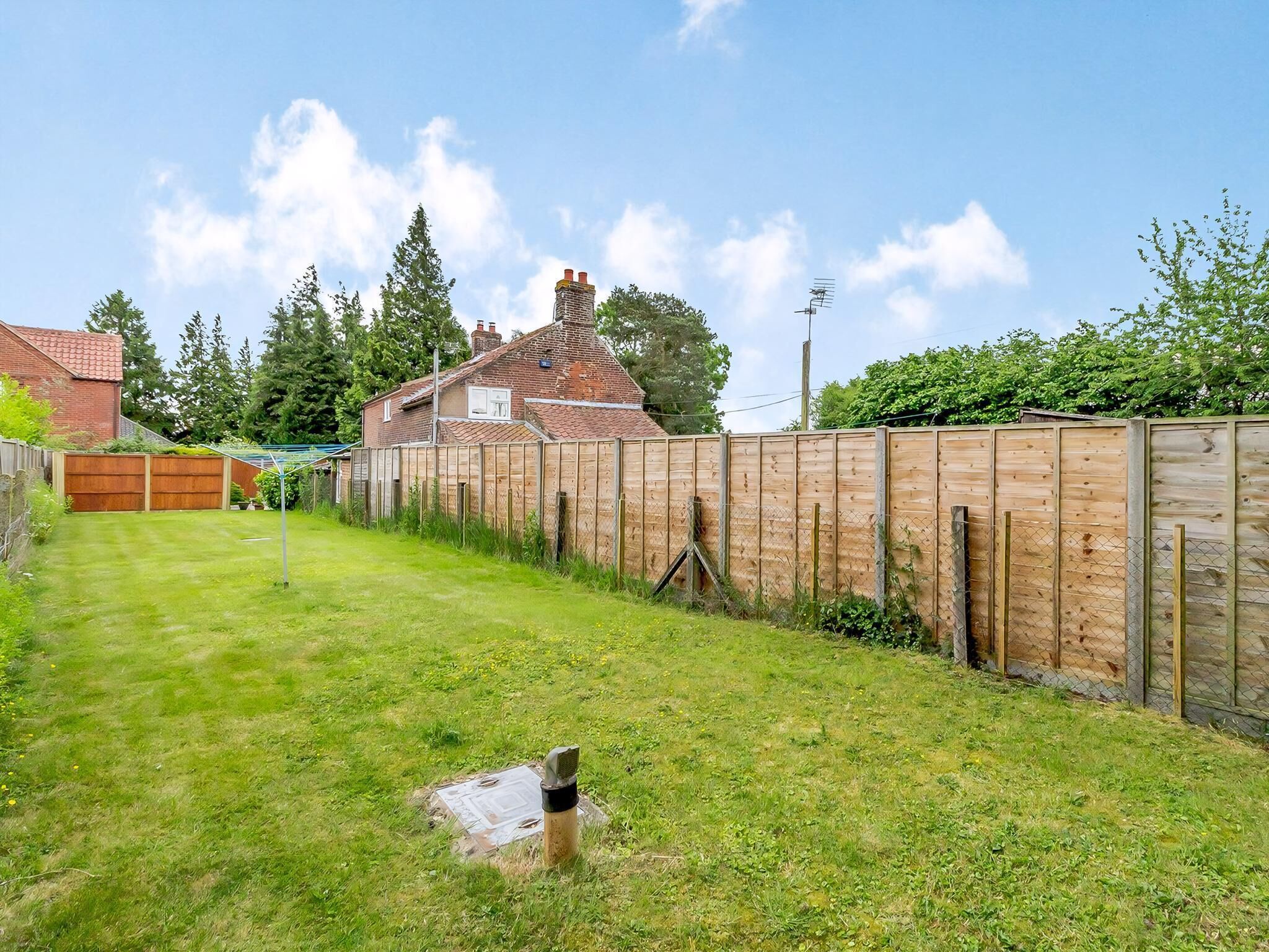 Un jardin avec une clôture en bois, une pelouse verdoyante et une maison en arrière-plan.