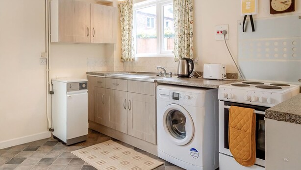 Een kleine keuken met een wasmachine, een fornuis en een spoelbak.
