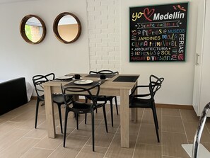 Un comedor con mesa de madera y sillas negras, dos espejos redondos en la pared y un letrero de pizarra con varias palabras.