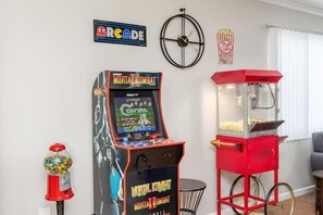 A retro arcade with a Mortal Kombat game, a gumball machine, and a popcorn machine in a room with a clock and a popcorn sign on the wall.