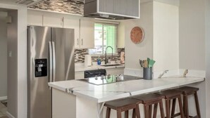 A modern kitchen with a stainless steel refrigerator, a built-in dishwasher, a white marble countertop, and wooden bar stools. - Heated Pool/Hot tub in heart of Tempe/ASU/Scottsdale (Tempe)