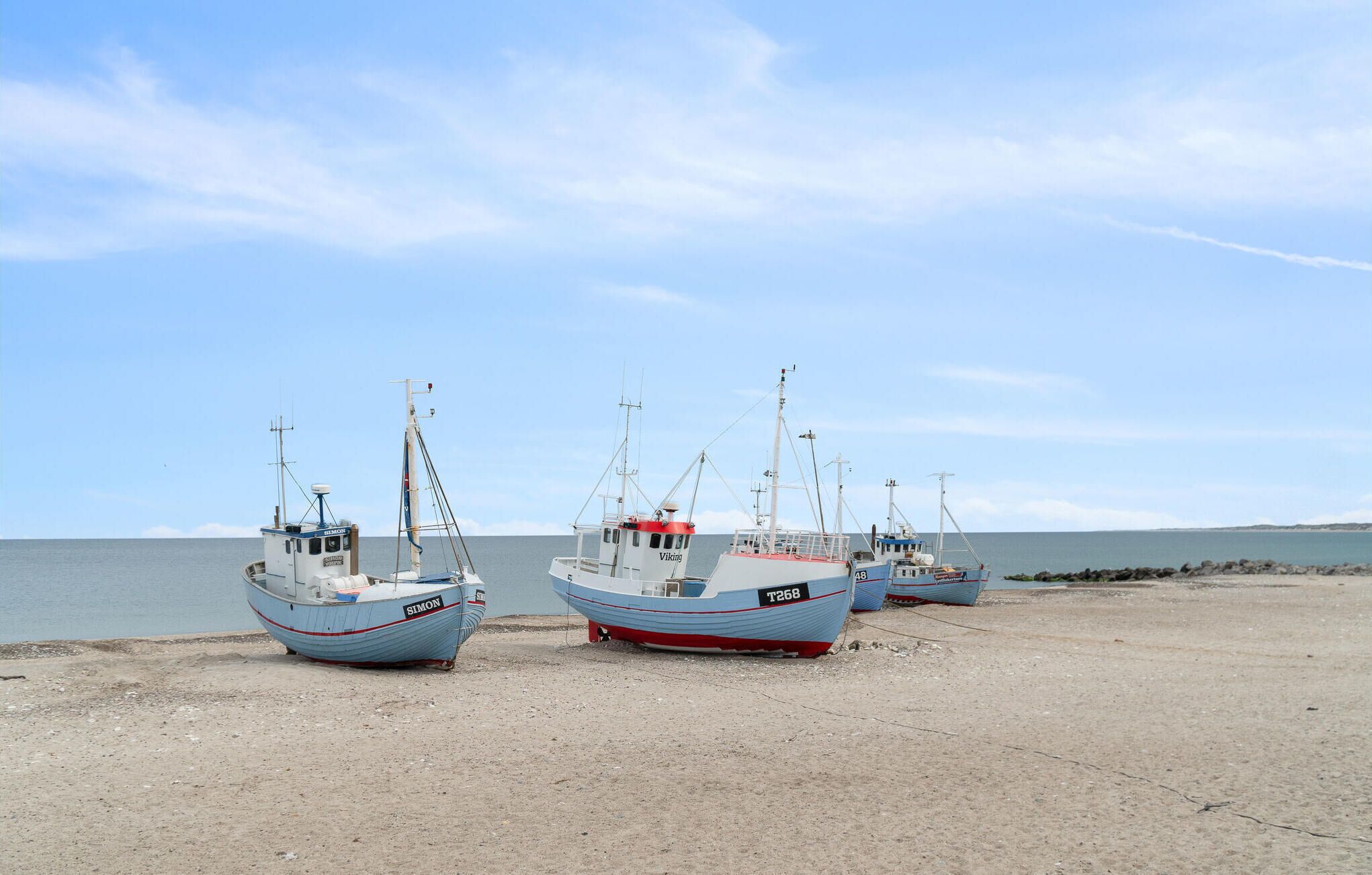 Three fishing boats on a sandy beach with calm water in the background.
